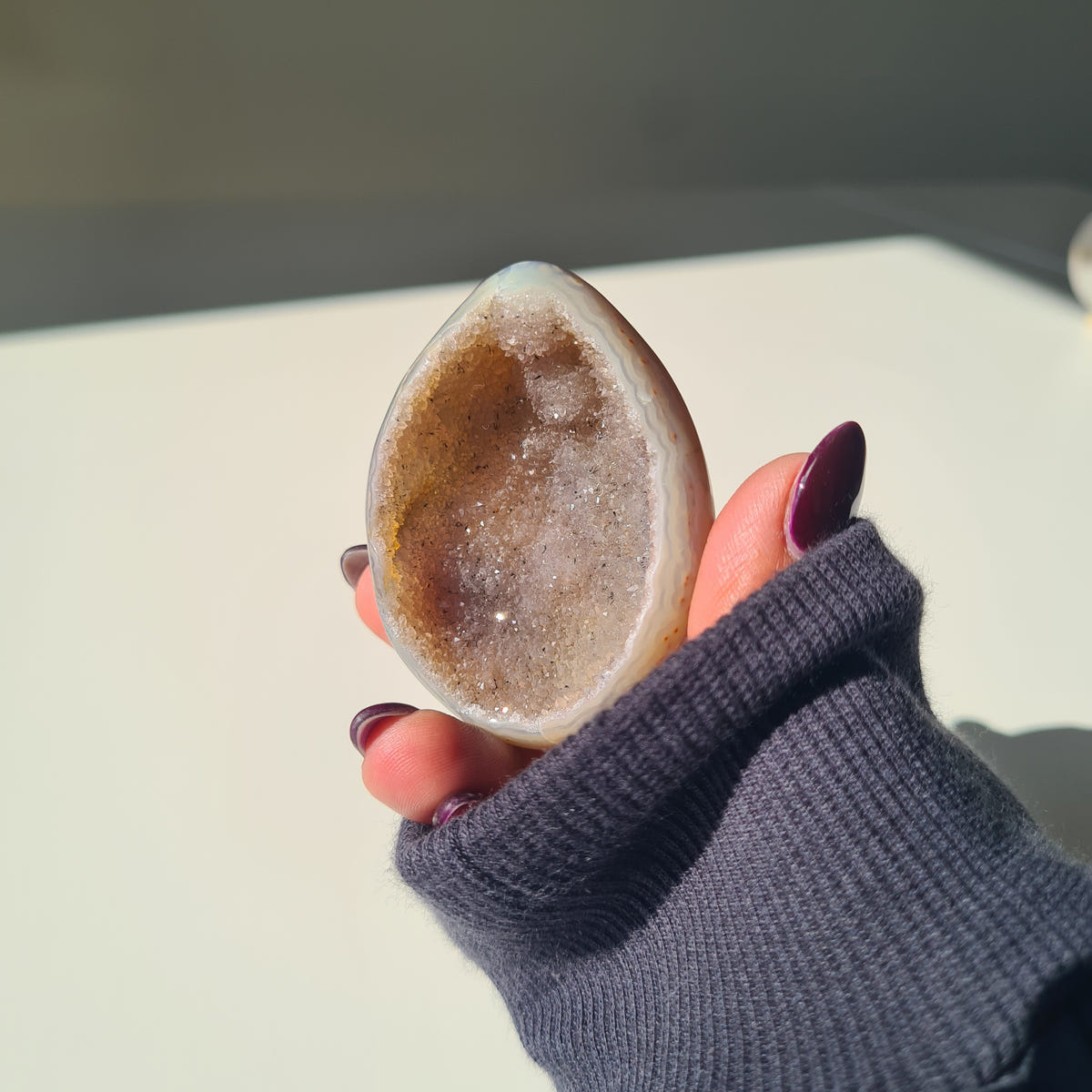 Agate geode egg with a golden-brown crystal-lined centre, held in a hand.