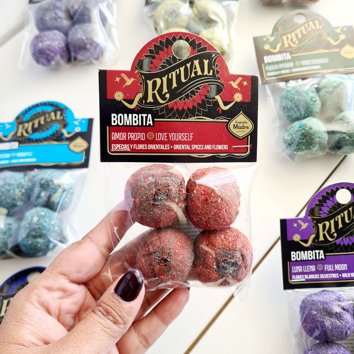 Hand holding a Love Yourself Ritual Bombita packet with four red botanical incense pieces.