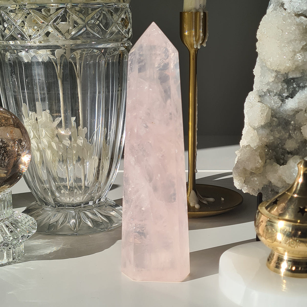 Tall translucent pink rose quartz point with pale cloudy inclusions beside glassware and a brass burner.