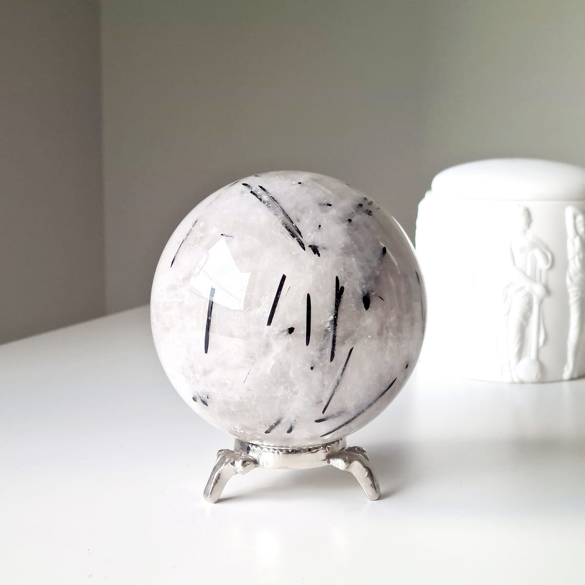 Tourmalinated quartz sphere with black needle-like inclusions in pale quartz, displayed on a silver-coloured stand.