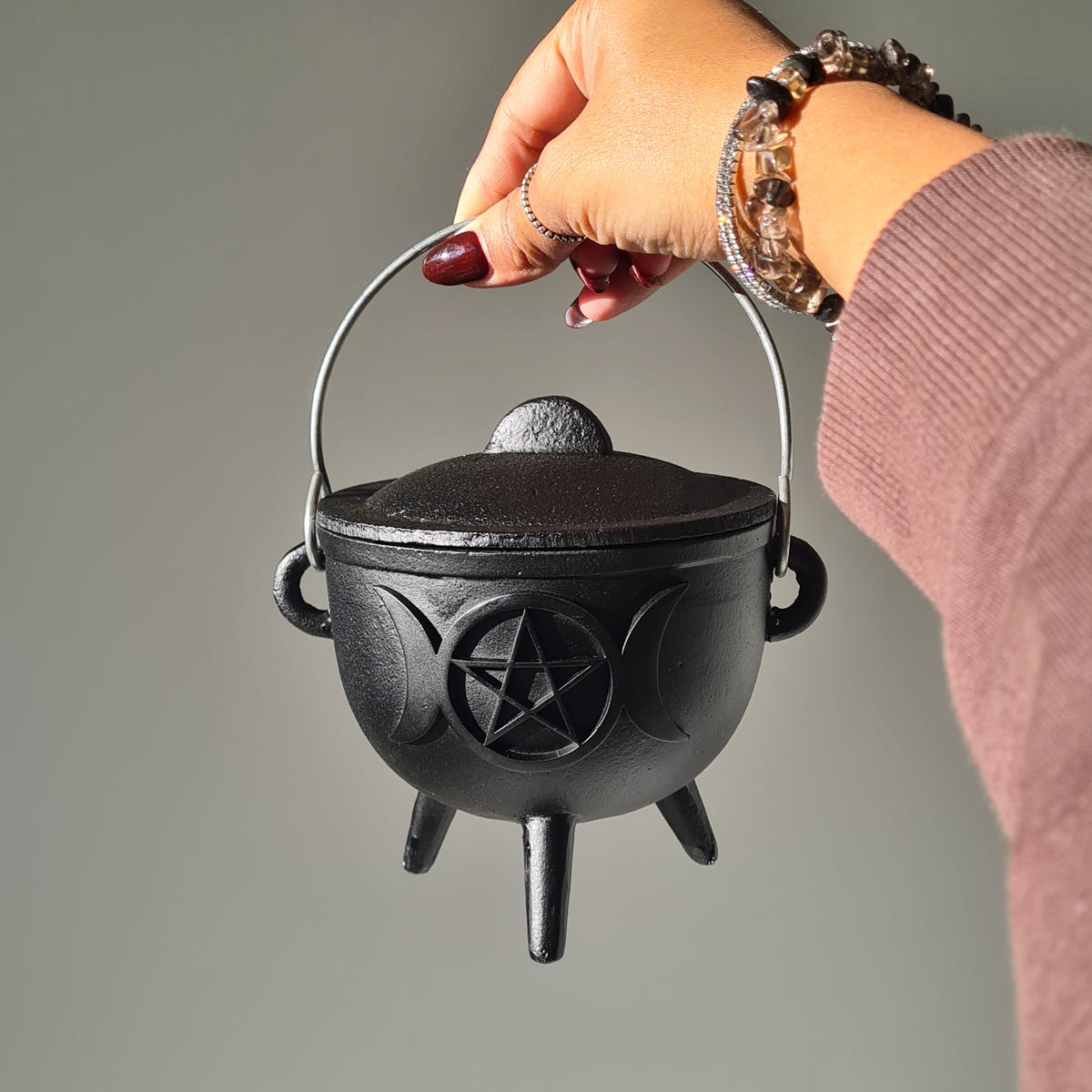 Black triple moon cauldron with a pentagram motif and fitted lid, shown with its handle raised.