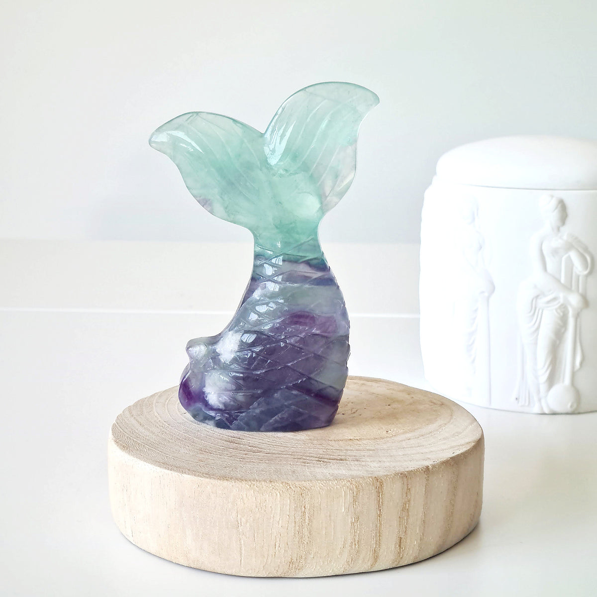 Pale green and purple fluorite mermaid tail carving on a round wooden display.