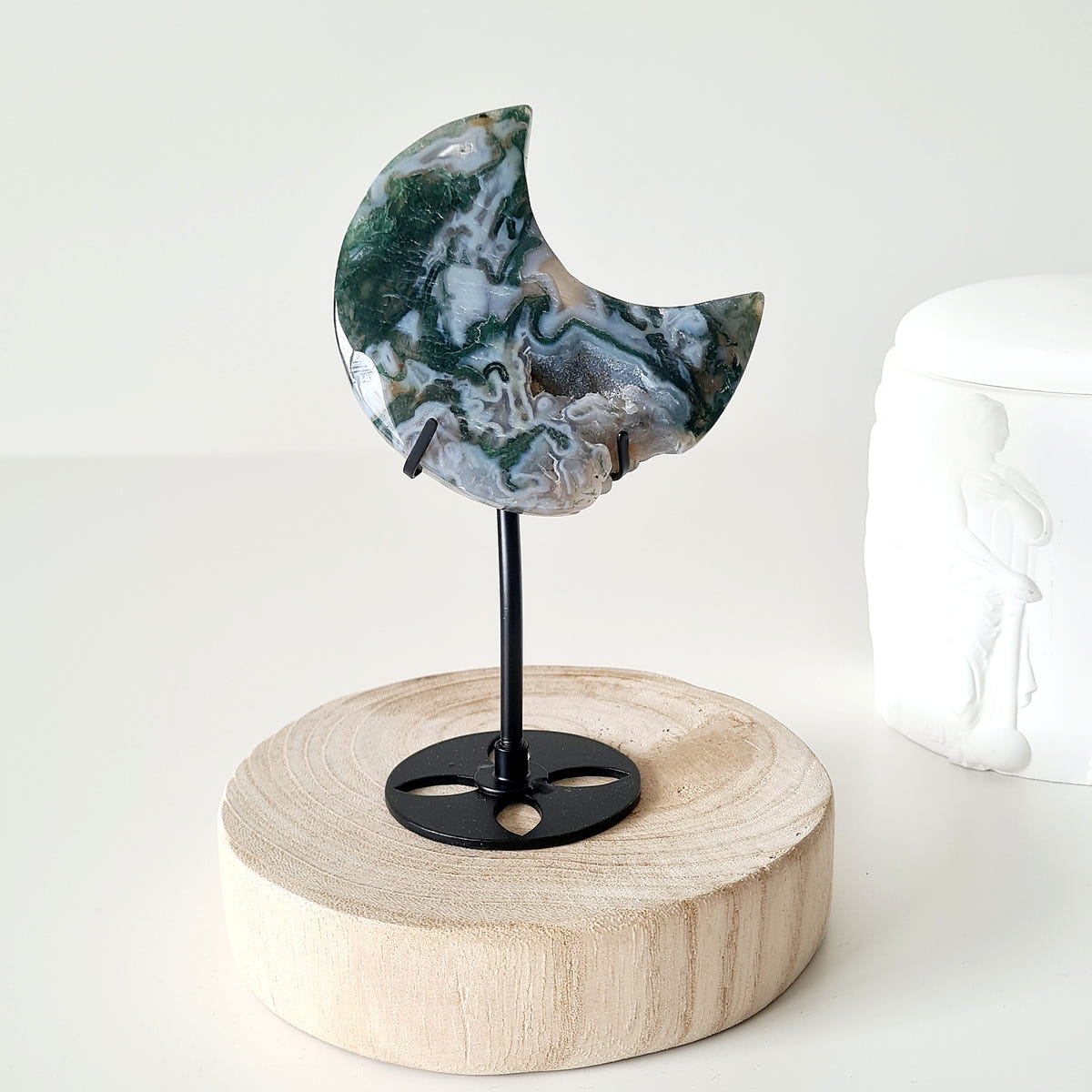 Moss agate Luna 10 crescent moon with swirling green, cream and grey patterns on a black stand.