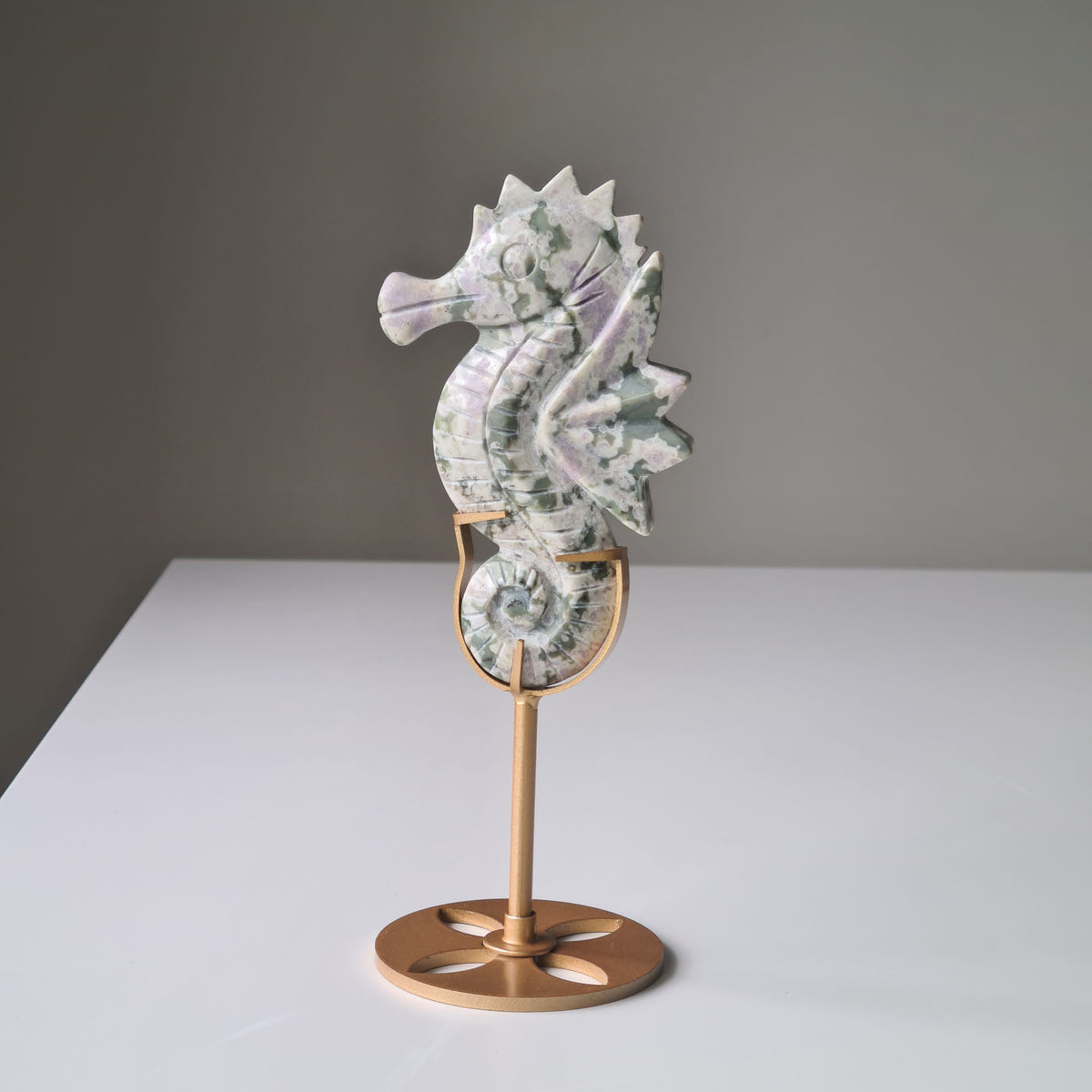 Peace jade seahorse carving B with pale green and lavender patterns, displayed on a gold-coloured stand.
