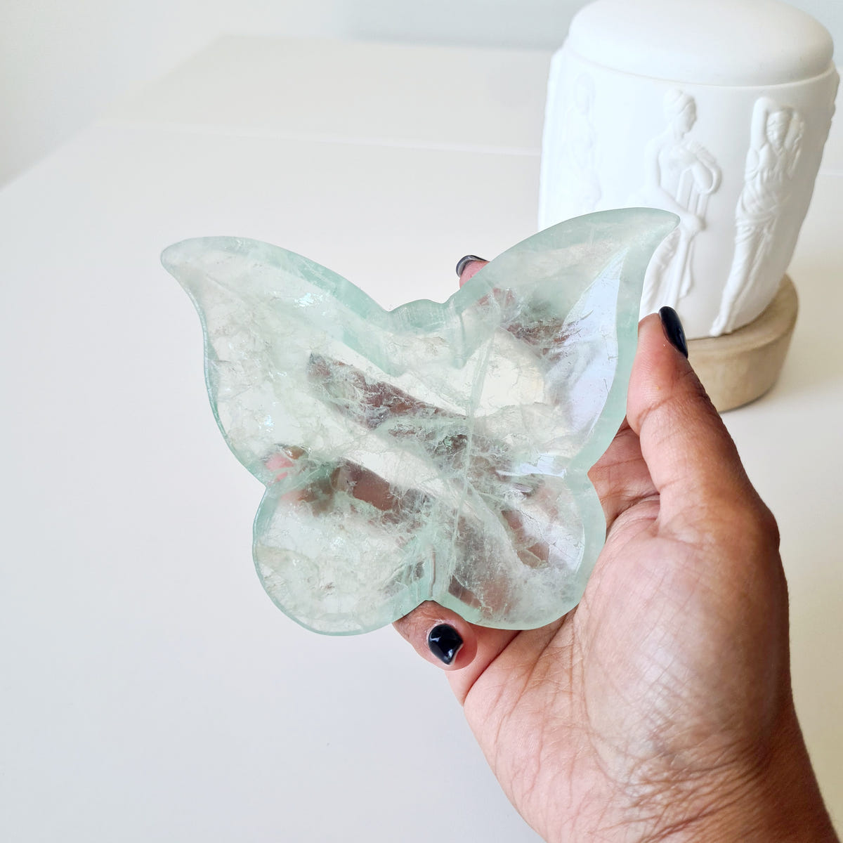 Hand holding fluorite butterfly bowl 05 with a pale green outline and white veils across the wings.