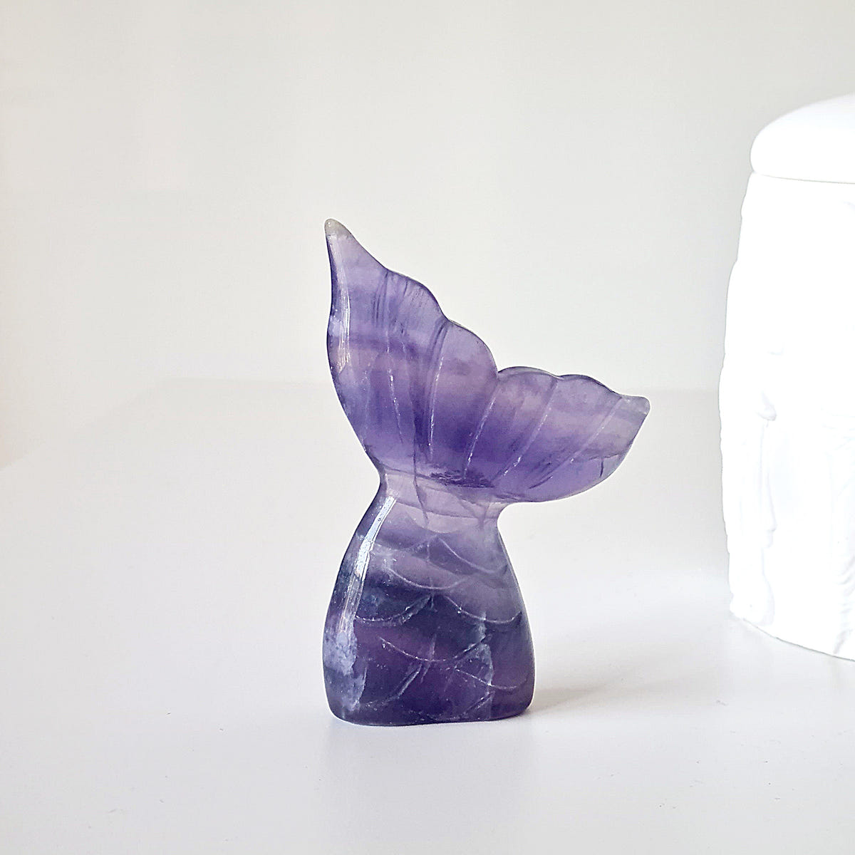 Lilac fluorite mermaid tail E with curved fins and deep purple bands across its polished surface.