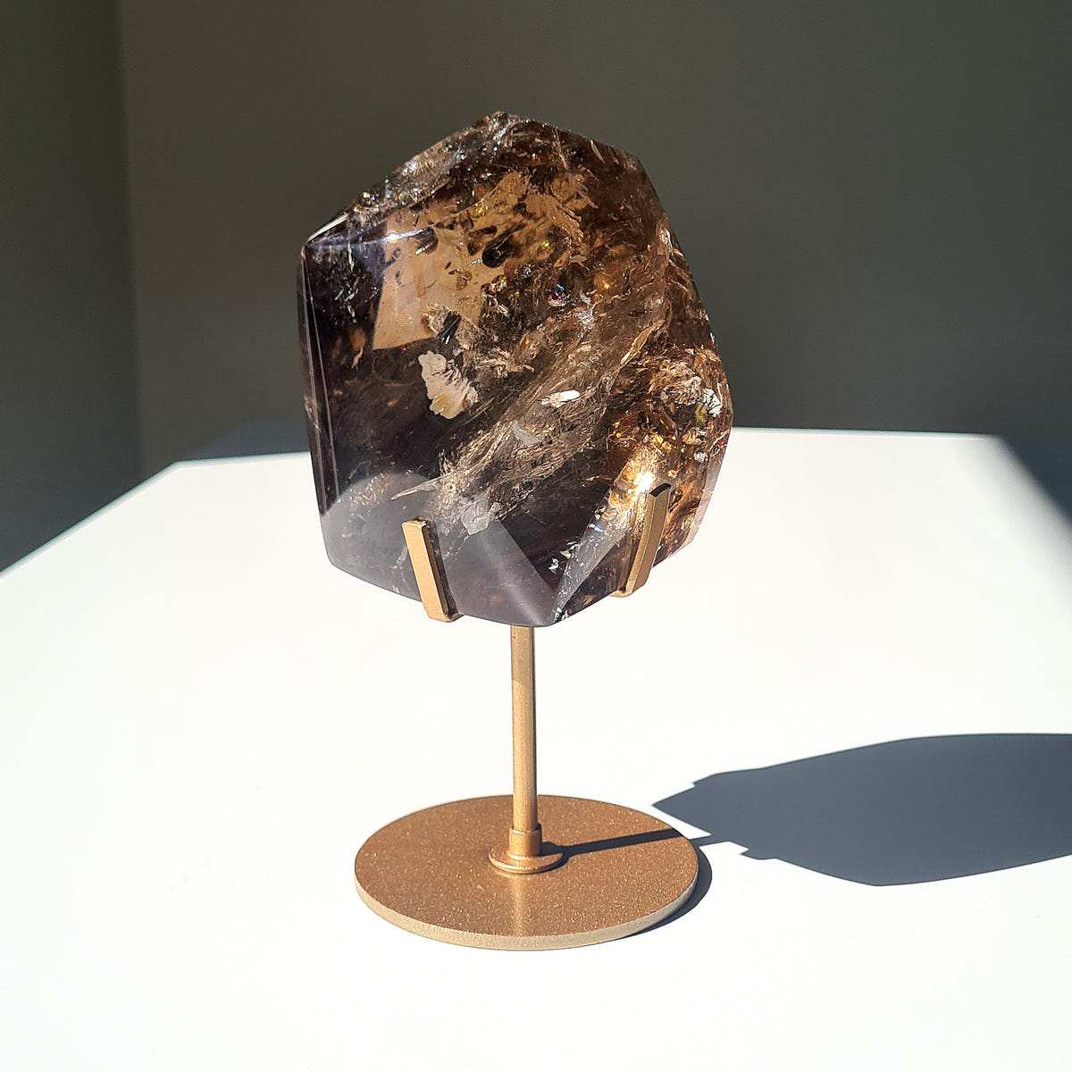 Polished smoky quartz freeform with deep brown and golden inclusions on a gold-coloured stand.