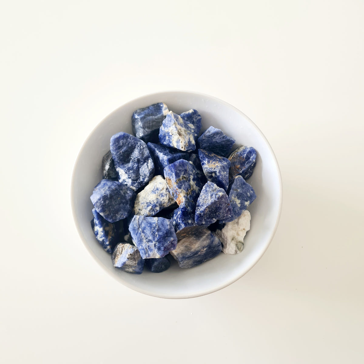 Small rough sodalite pieces with deep blue and white surfaces arranged in a white bowl.