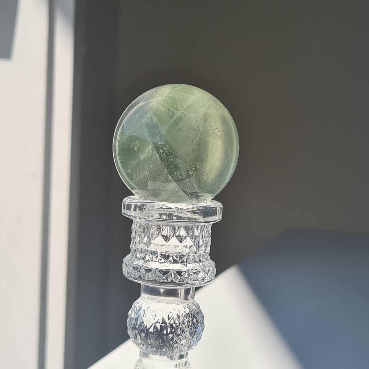 Close view of a pale green fluorite sphere with translucent bands on a clear stand.