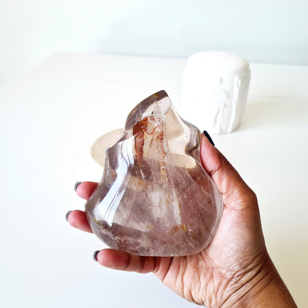 Hand holding a polished quartz flame with smoky tones and natural inclusions.