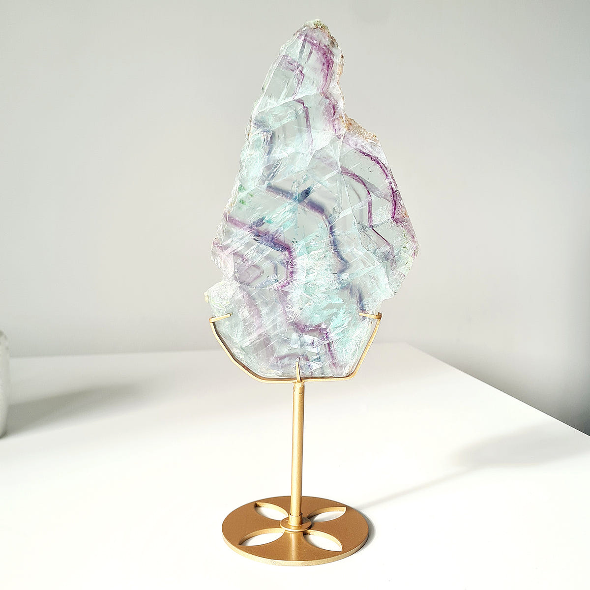 Pale green Fluorite slab with curved purple bands displayed on a gold-coloured stand.