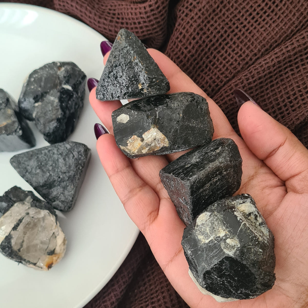 Hand holding rough black tourmaline pieces with dark angular surfaces and pale mineral patches.