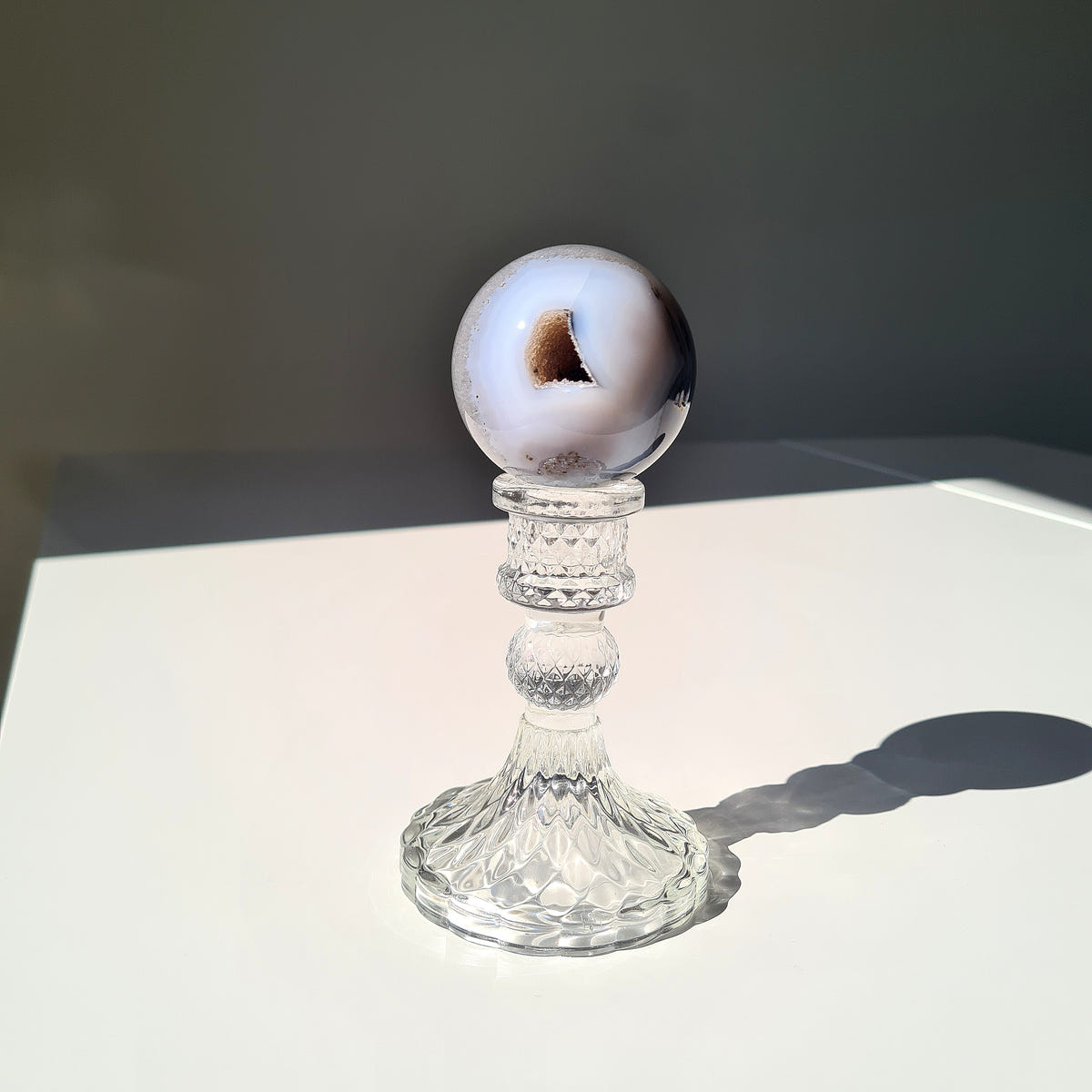 White and grey Agate geode sphere with a small dark opening on a clear pedestal.