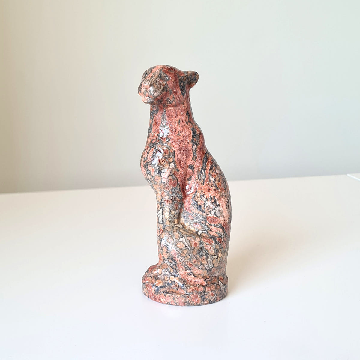 Jasper leopard carving C with pink, grey and black mottling, seated upright on an oval base.