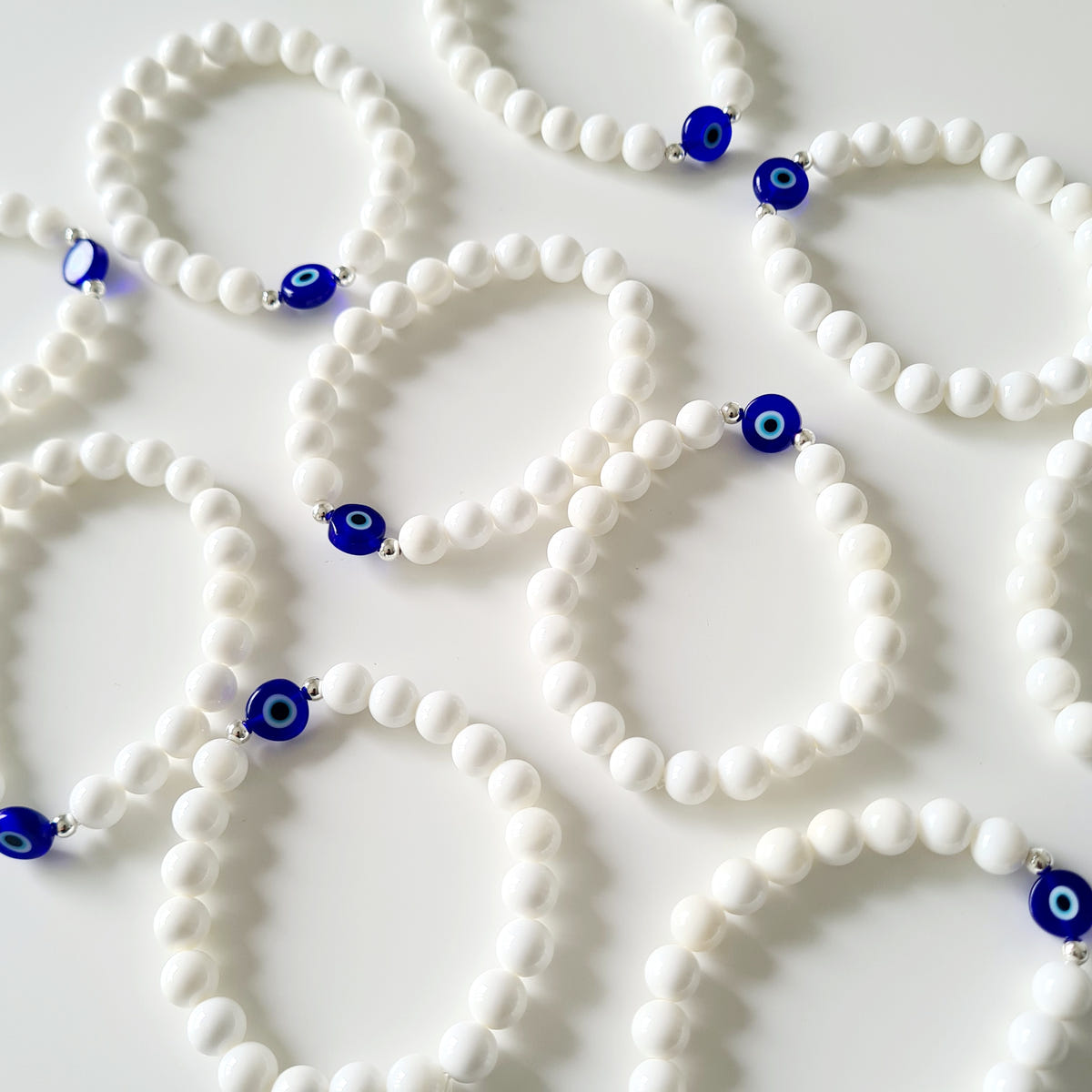 White mother-of-pearl beaded bracelets with blue and white evil eye beads arranged on a pale surface.