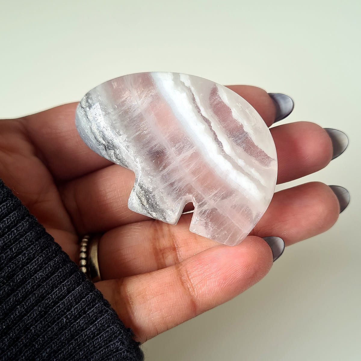 Hand holding a small quartz and pyrite Zuni bear carving with pale pink, white and grey bands.