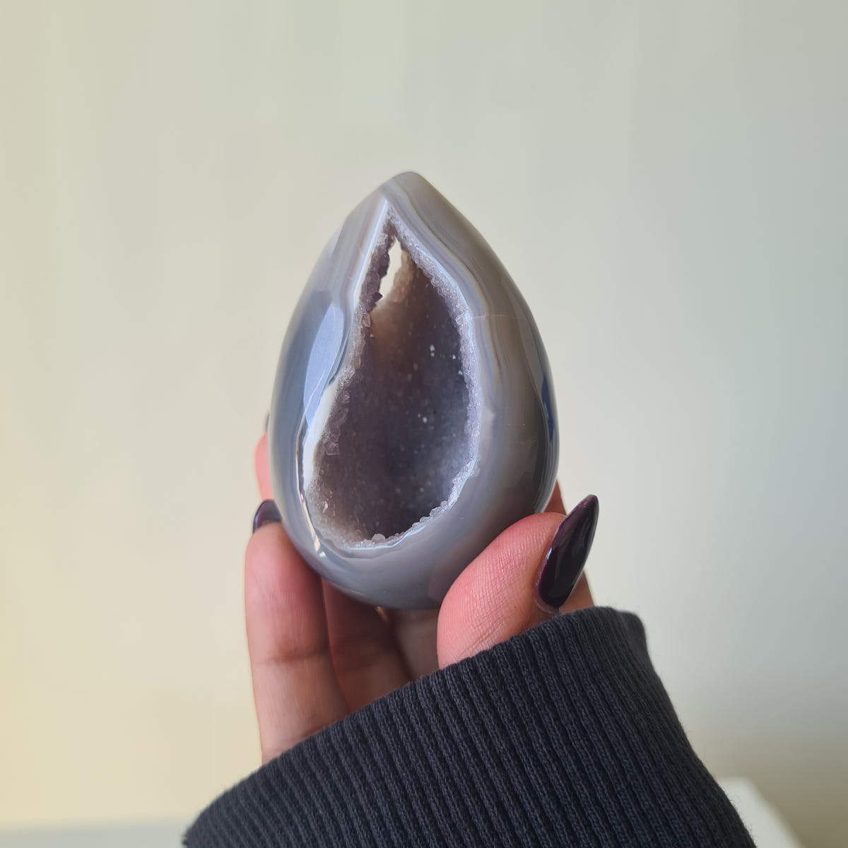 Hand holding a grey Agate geode egg with a pointed, crystal-lined opening.