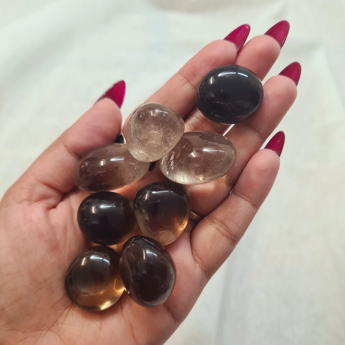 Hand holding smooth smoky quartz tumbles in translucent brown, amber and nearly black tones.