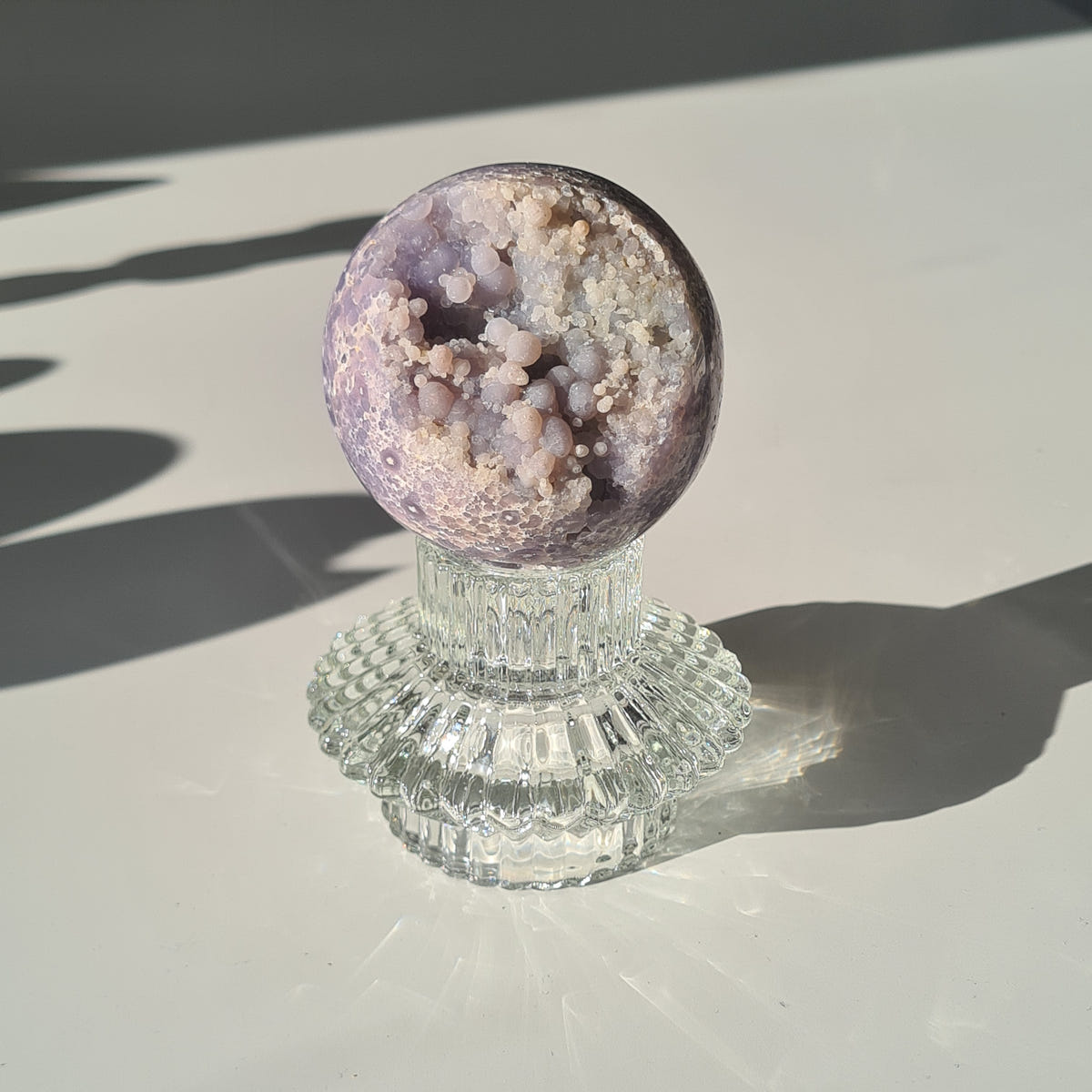 Purple grape agate sphere with pale clustered areas on a clear footed glass stand.