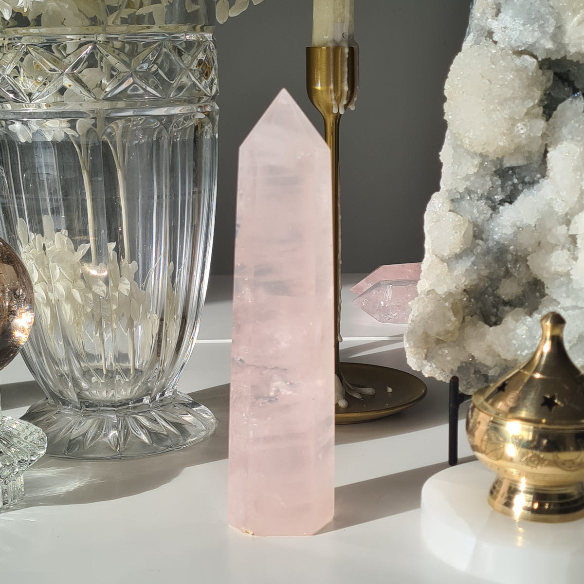 Star Dust rose quartz tower with pale horizontal bands, displayed beside glassware and an agate geode.