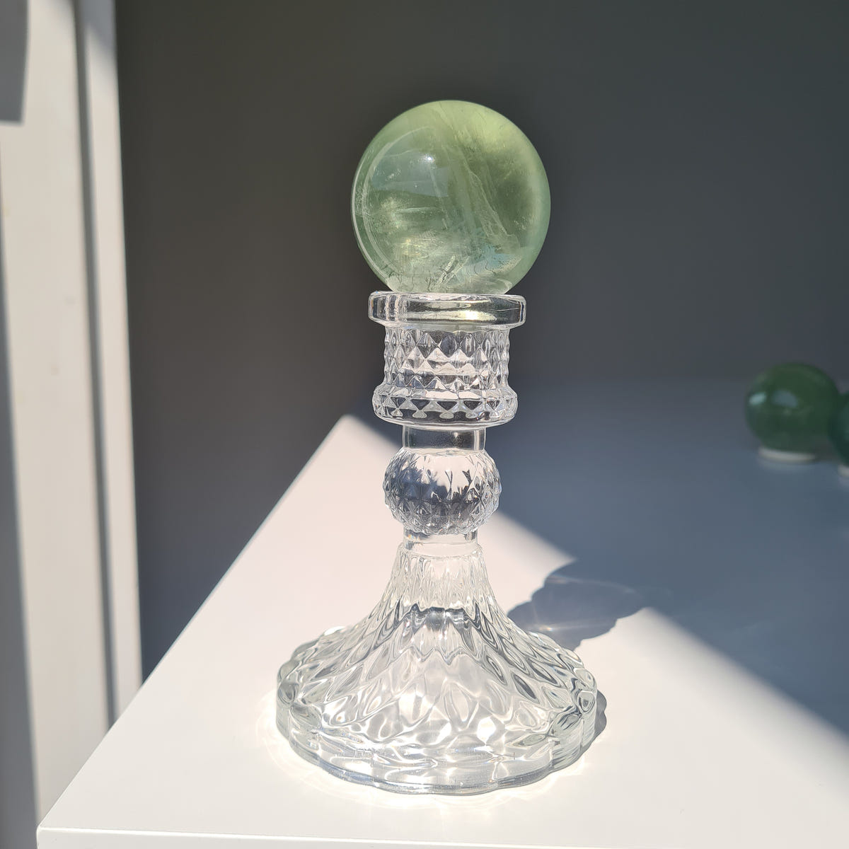 Pale green Frozen Lake fluorite sphere A on a tall clear decorative stand, lit from the side.