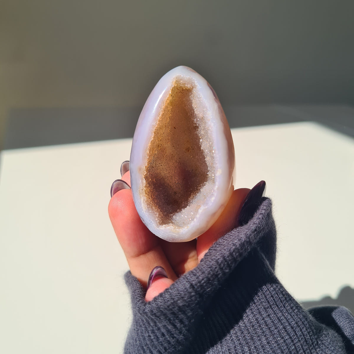 Hand holding an Agate geode egg with a pale rim and warm brown crystal pocket.