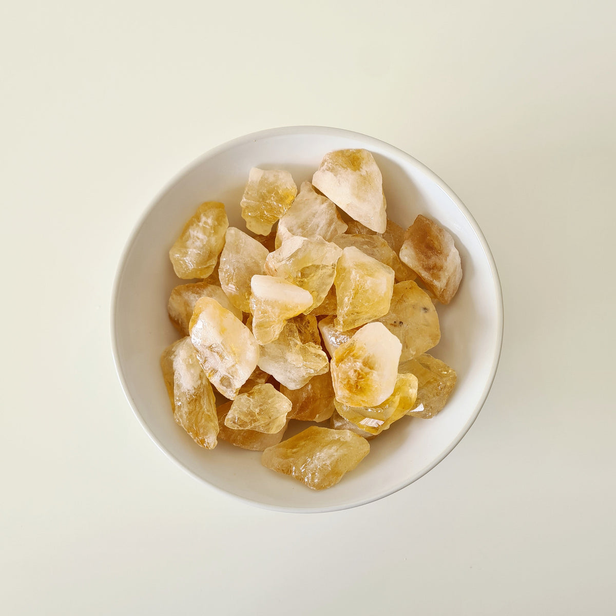 Small rough heated citrine pieces in pale yellow and gold arranged in a white bowl.