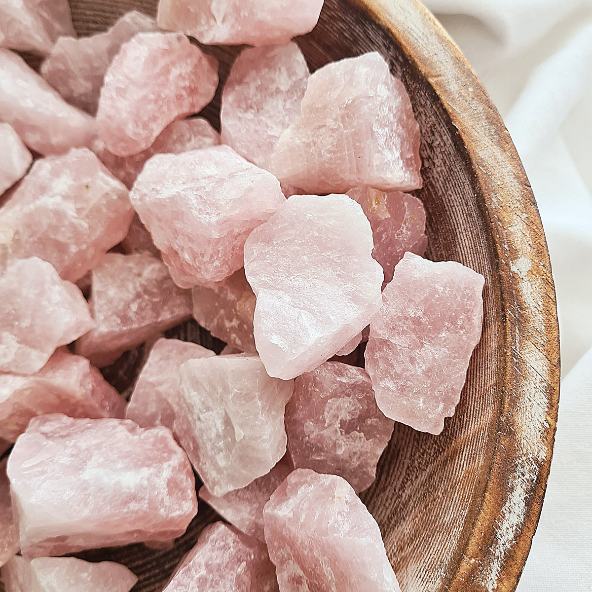 Rough pale pink rose quartz pieces arranged closely together in a wooden bowl.