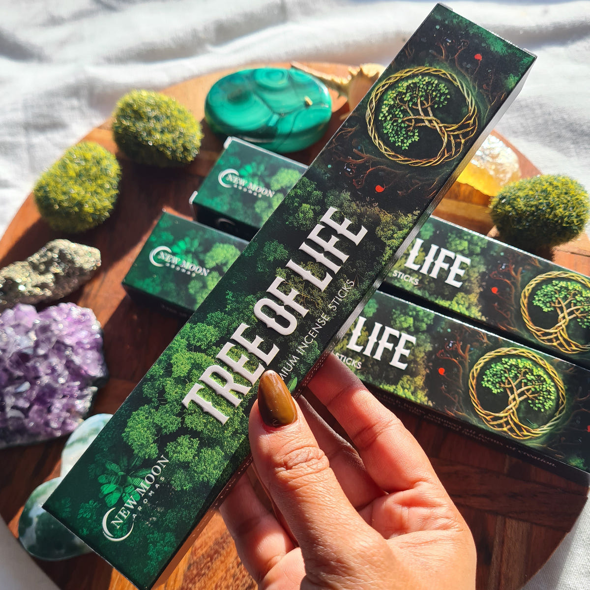 Hand holding a Tree of Life incense packet above matching boxes, crystals and ritual pieces.