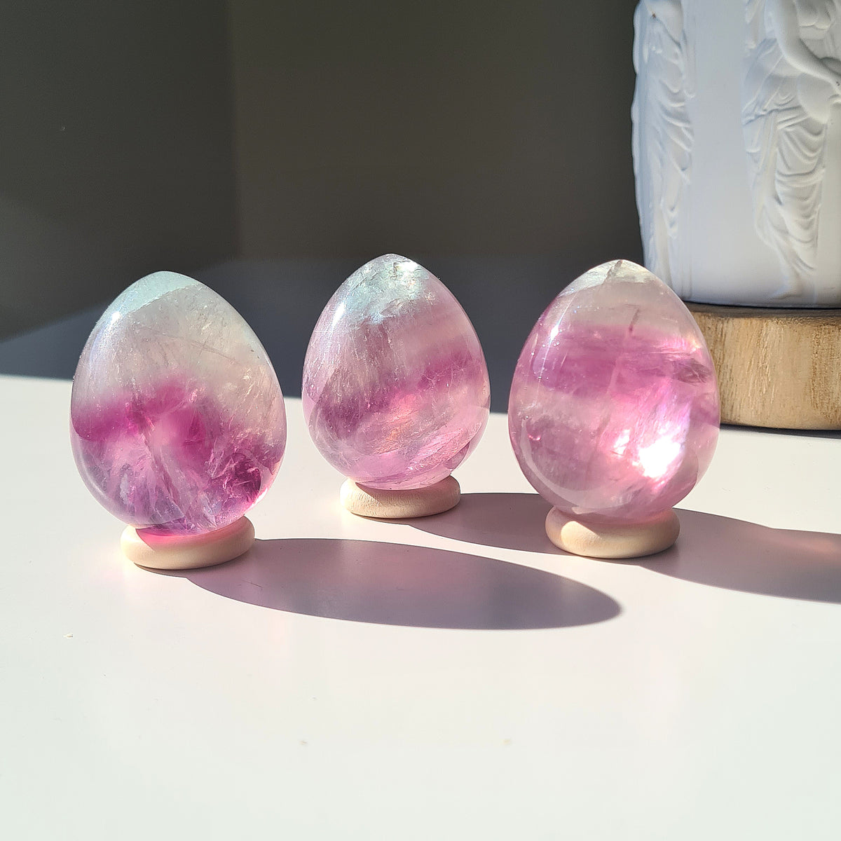 Three gemmy Fluorite eggs with pink and purple bands displayed in sunlight.