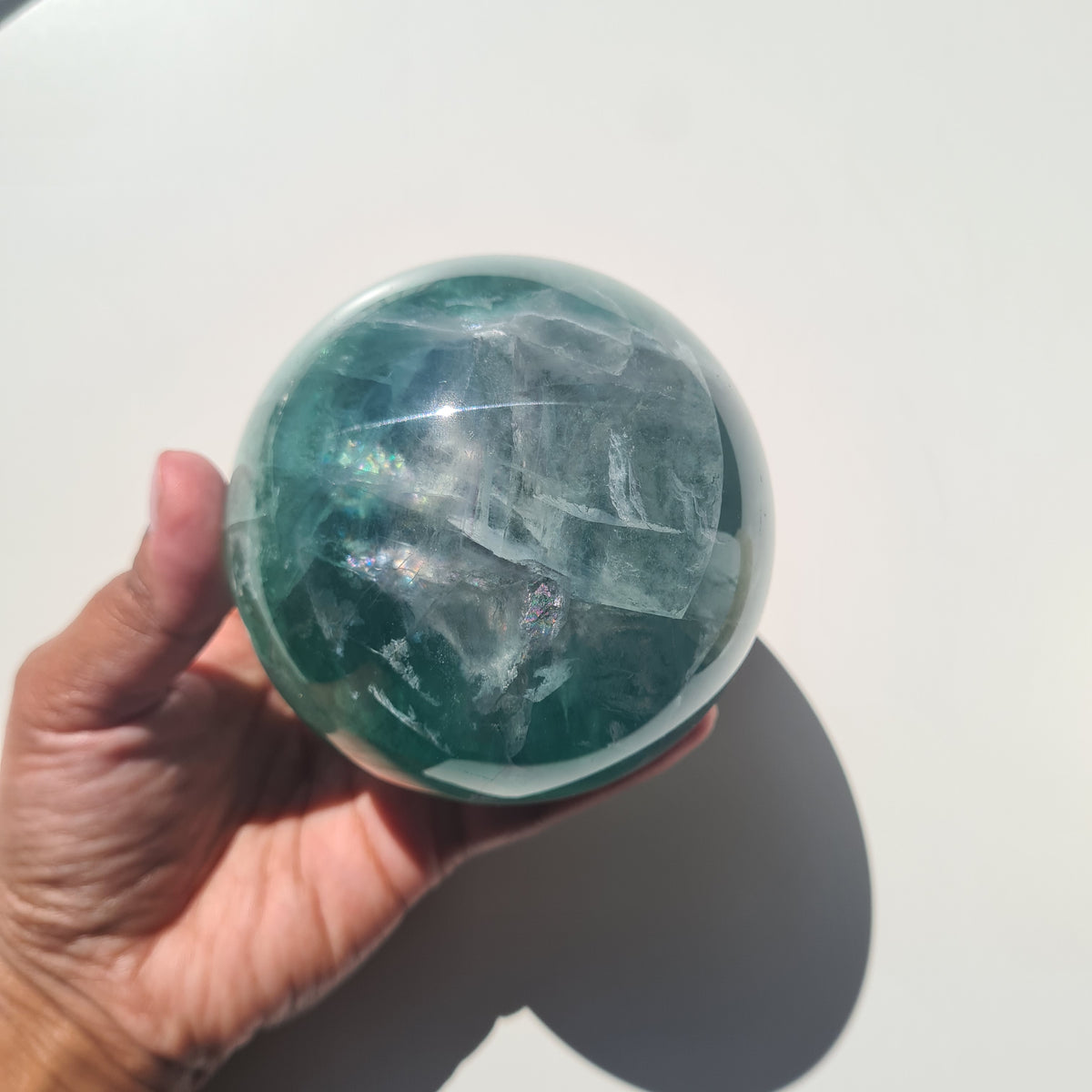 Green Fluorite sphere, 8.4 cm, with translucent teal tones and natural internal formations, held in a hand.