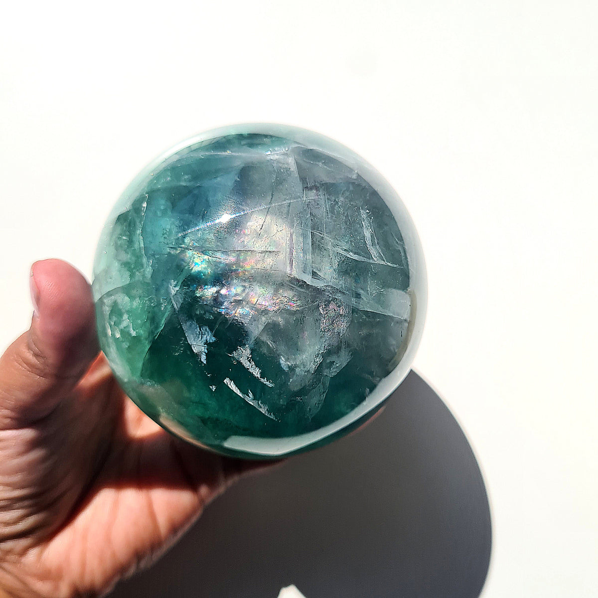Green Fluorite sphere, 8.4 cm, with translucent teal tones and natural internal formations, held in a hand.