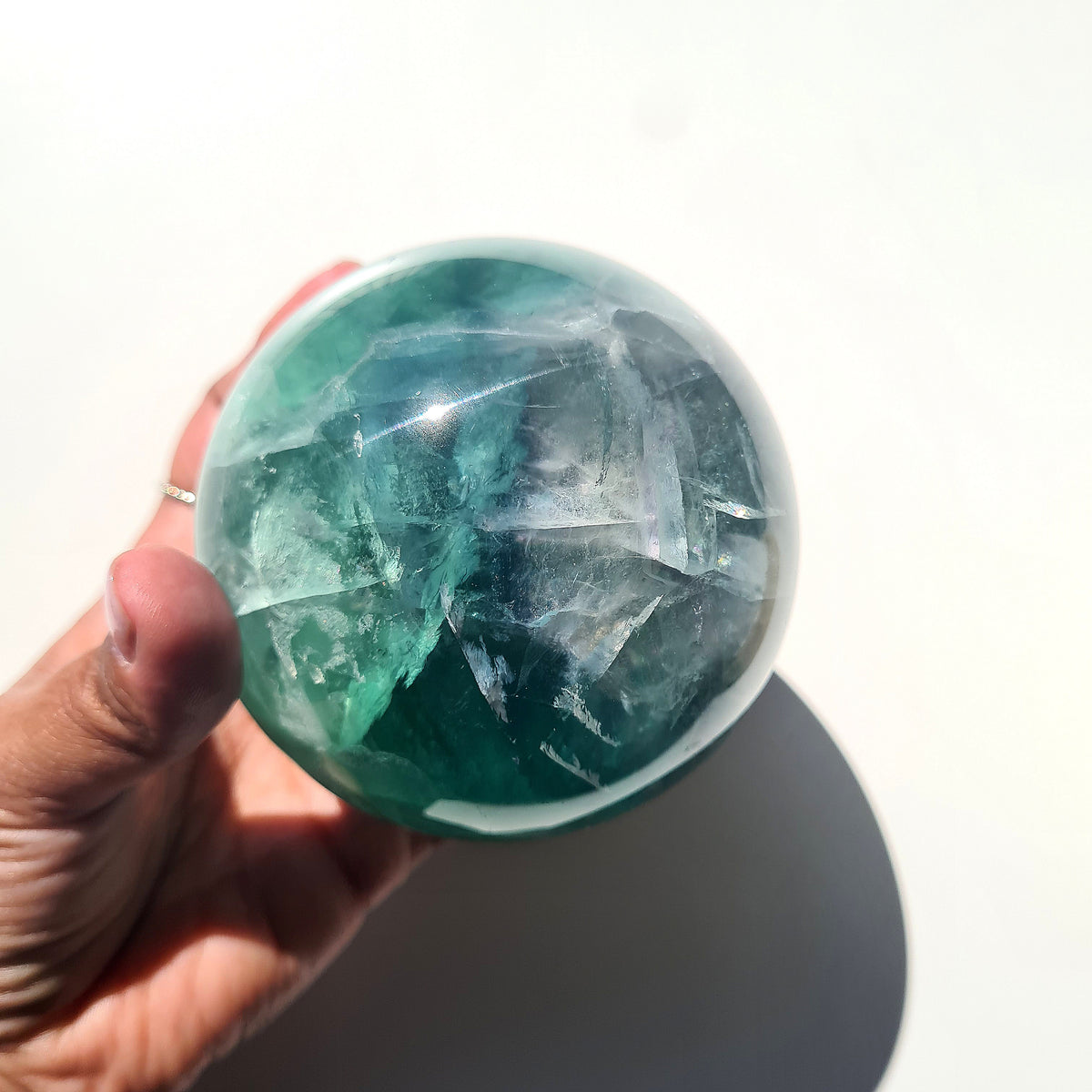 Green Fluorite sphere, 8.4 cm, with translucent teal tones and natural internal formations, held in a hand.