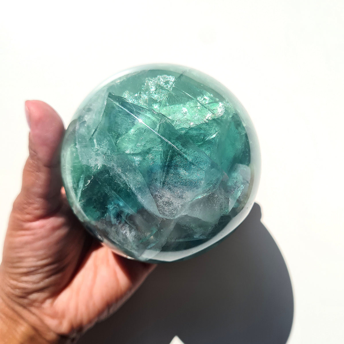 Green Fluorite sphere, 8.4 cm, with translucent teal tones and natural internal formations, held in a hand.