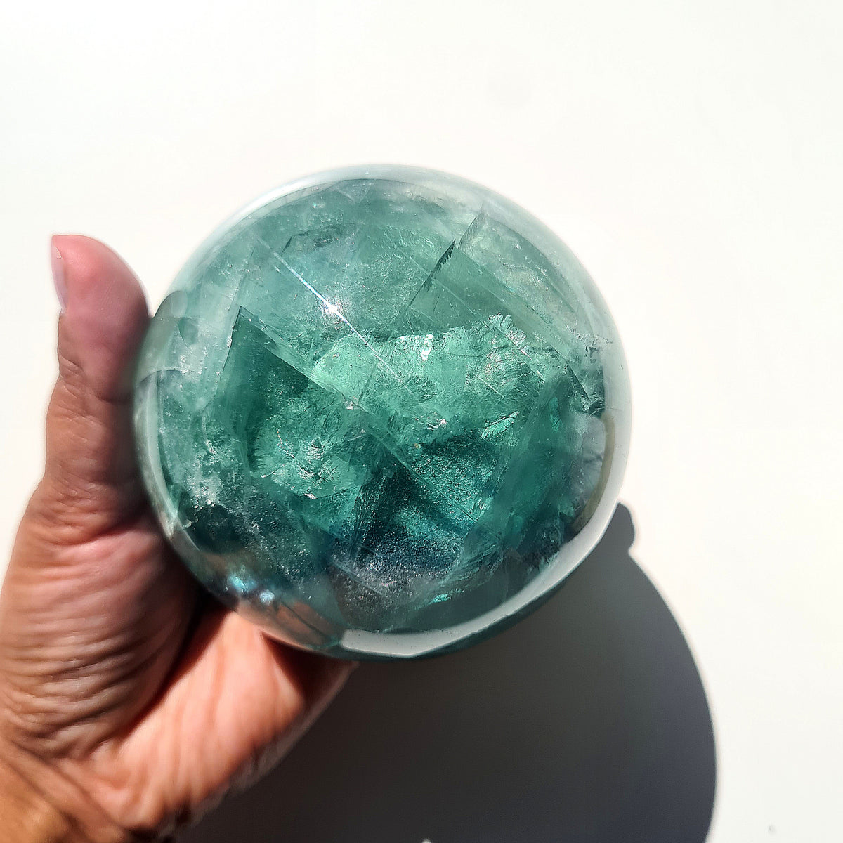 Green Fluorite sphere, 8.4 cm, with translucent teal tones and natural internal formations, held in a hand.