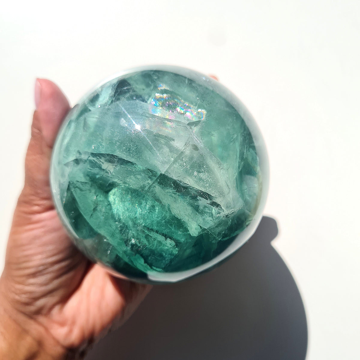 Green Fluorite sphere, 8.4 cm, with translucent teal tones and natural internal formations, held in a hand.