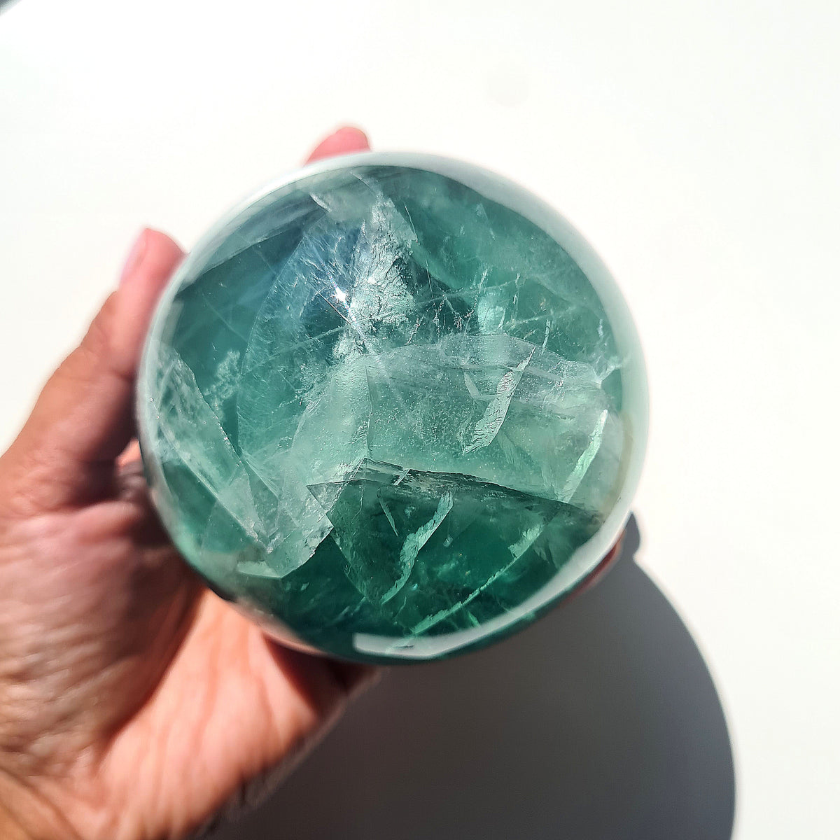 Green Fluorite sphere, 8.4 cm, with translucent teal tones and natural internal formations, held in a hand.