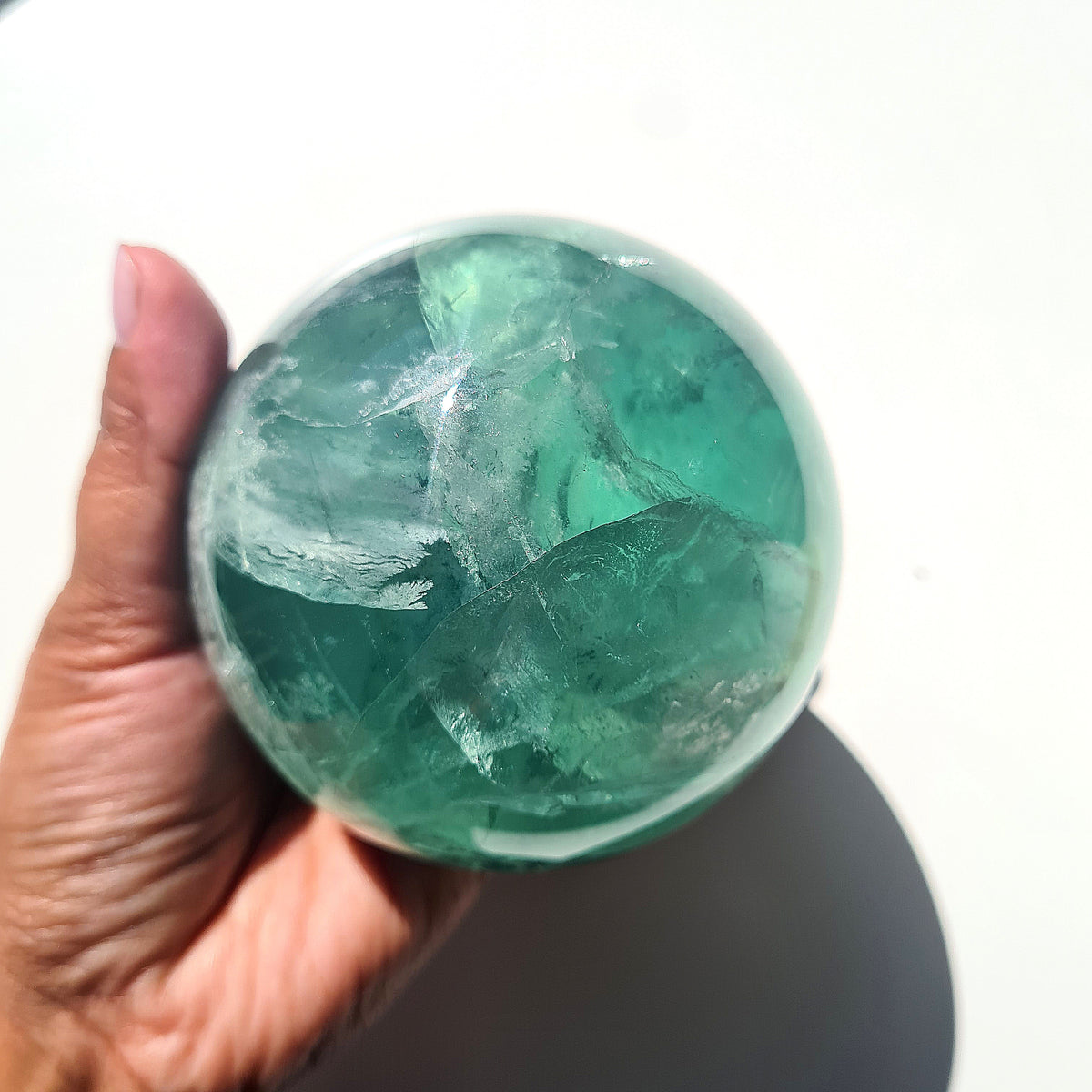 Green Fluorite sphere, 8.4 cm, with translucent teal tones and natural internal formations, held in a hand.