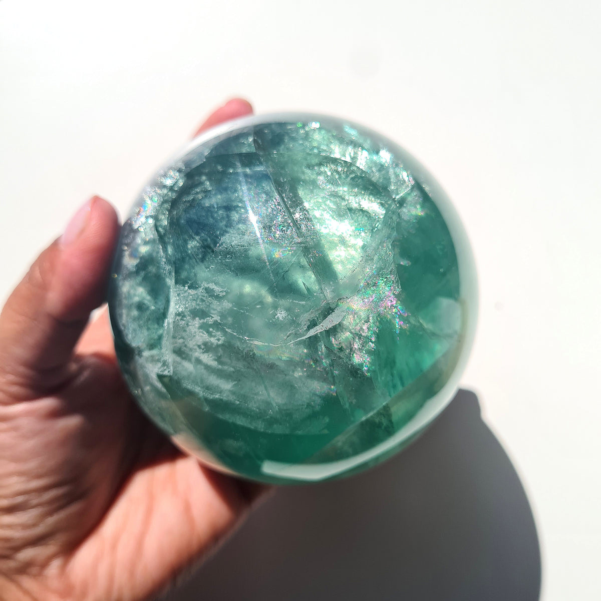 Green Fluorite sphere, 8.4 cm, with translucent teal tones and natural internal formations, held in a hand.
