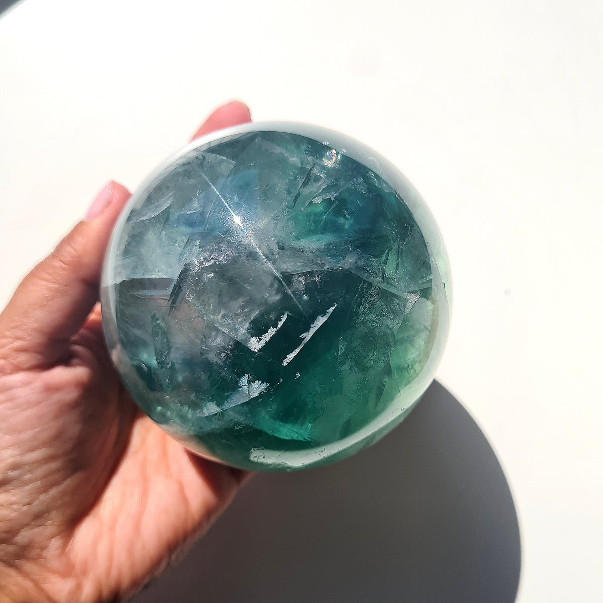 Green Fluorite sphere, 8.4 cm, with translucent teal tones and natural internal formations, held in a hand.