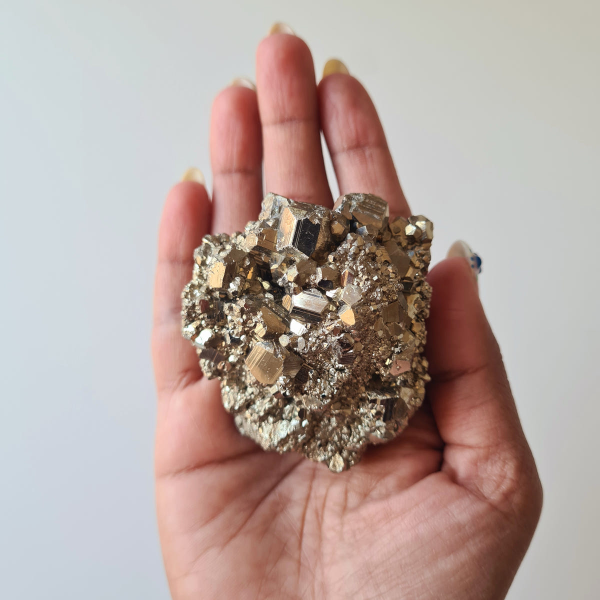 Hand holding pyrite specimen H with prominent angular crystal faces surrounded by smaller metallic clusters.