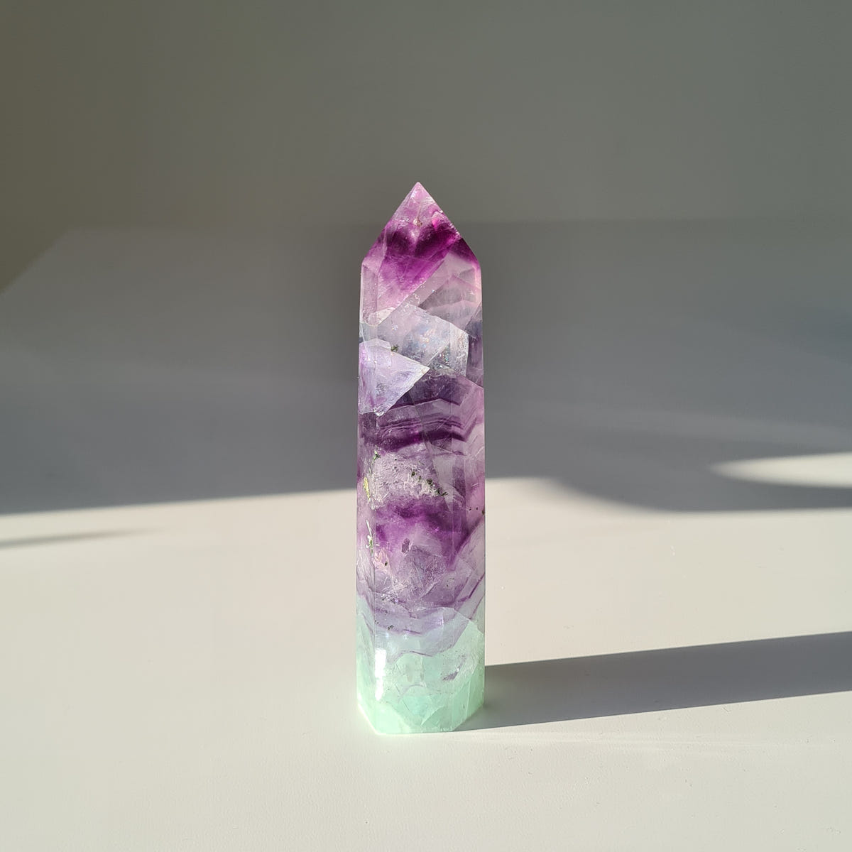 Dreamland fluorite point f11 with deep purple bands, cloudy pale sections and a mint-green base.