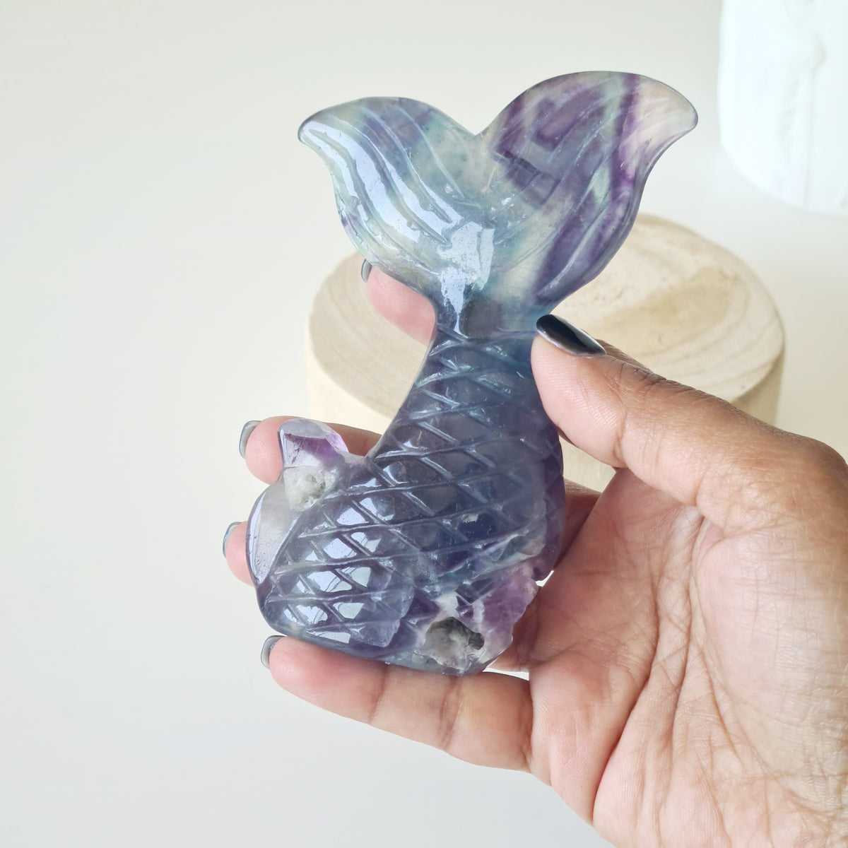 Hand holding a purple and green fluorite mermaid tail carving.