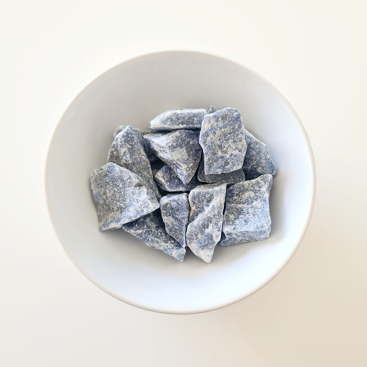 Rough blue aventurine stones with angular grey-blue surfaces arranged in a white bowl.