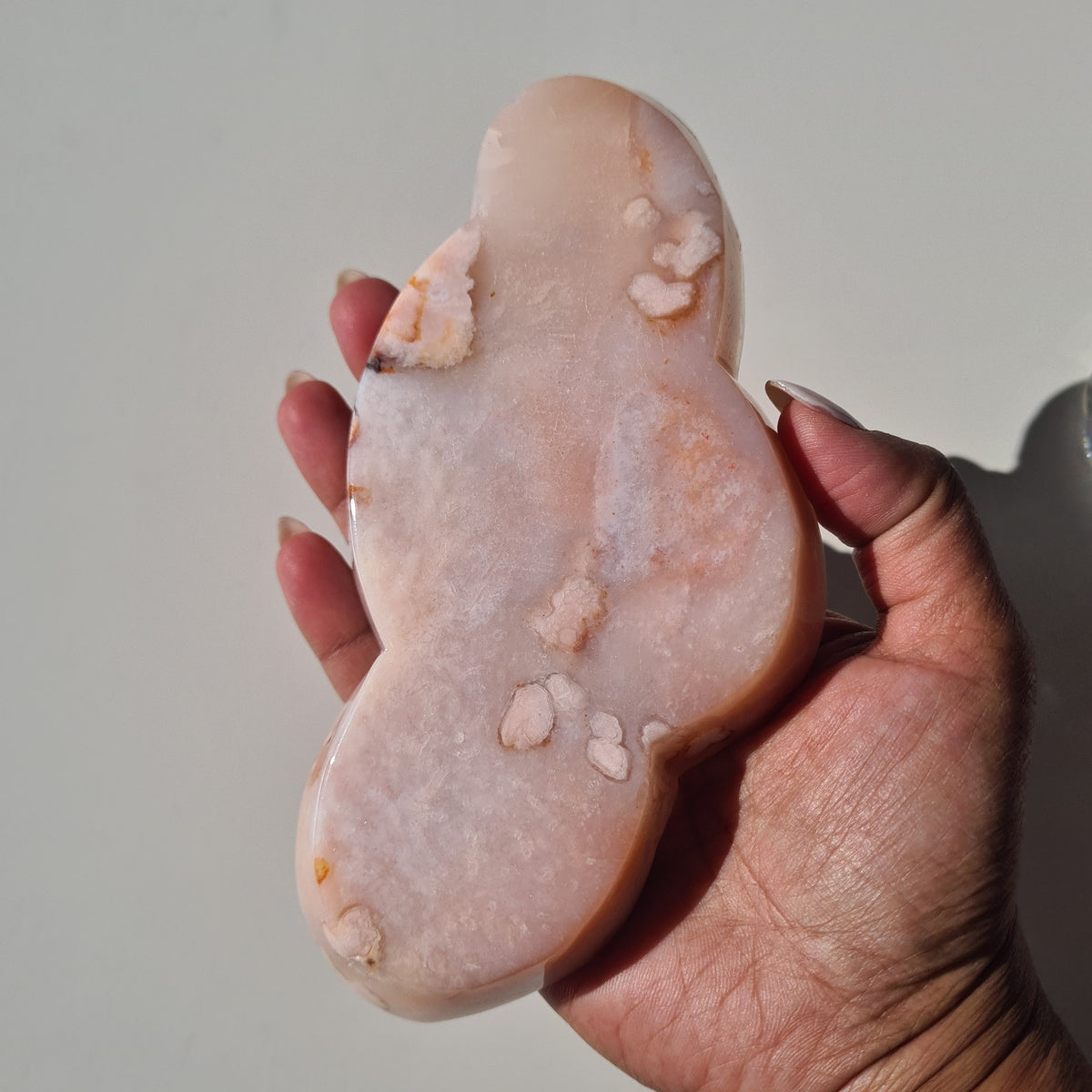 Hand holding a pale pink carnelian flower agate bowl with an irregular outline and white patterns.