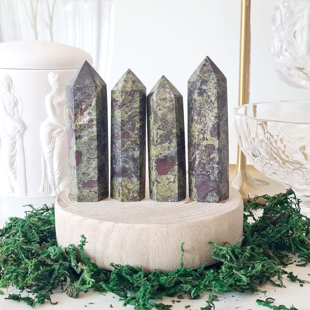 Four dragon’s blood crystal points with green and dark red patches displayed on a round wooden base.