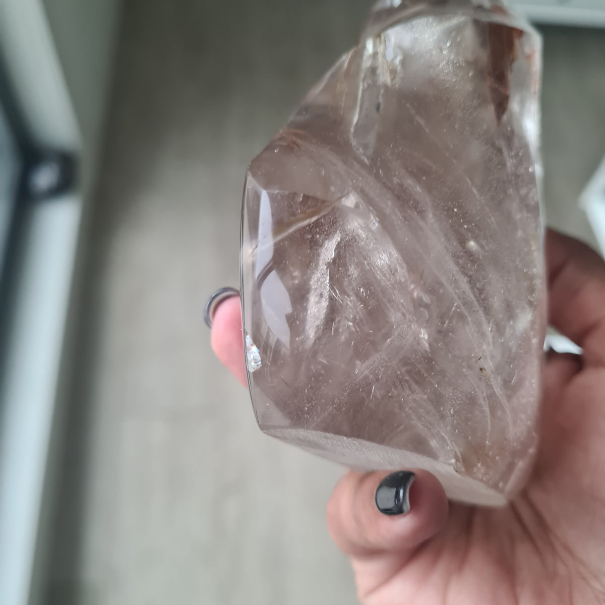 Hand holding a polished quartz flame with smoky tones and natural inclusions.