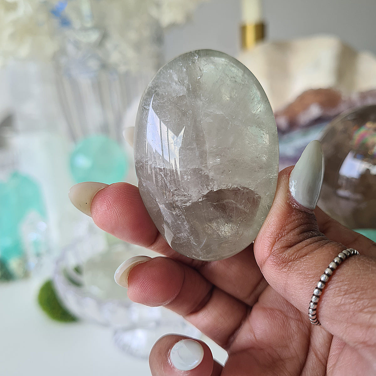 Hand holding oval green amethyst palm stone G17 with cloudy pale green sections and reflective internal lines.