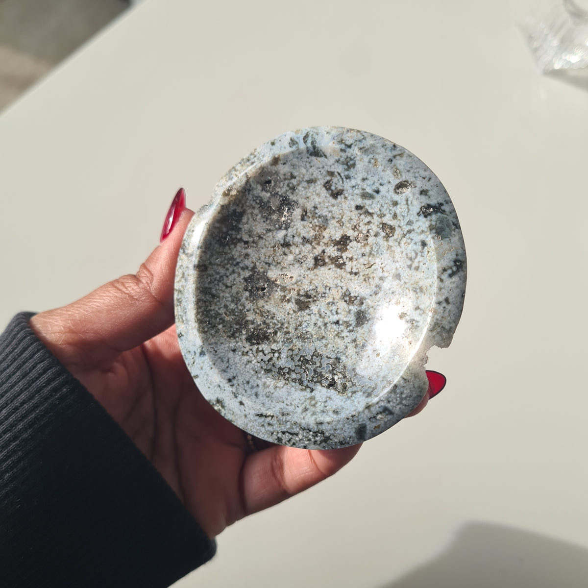 Hand holding a rounded ocean jasper bowl with fine grey, black and cream speckles.