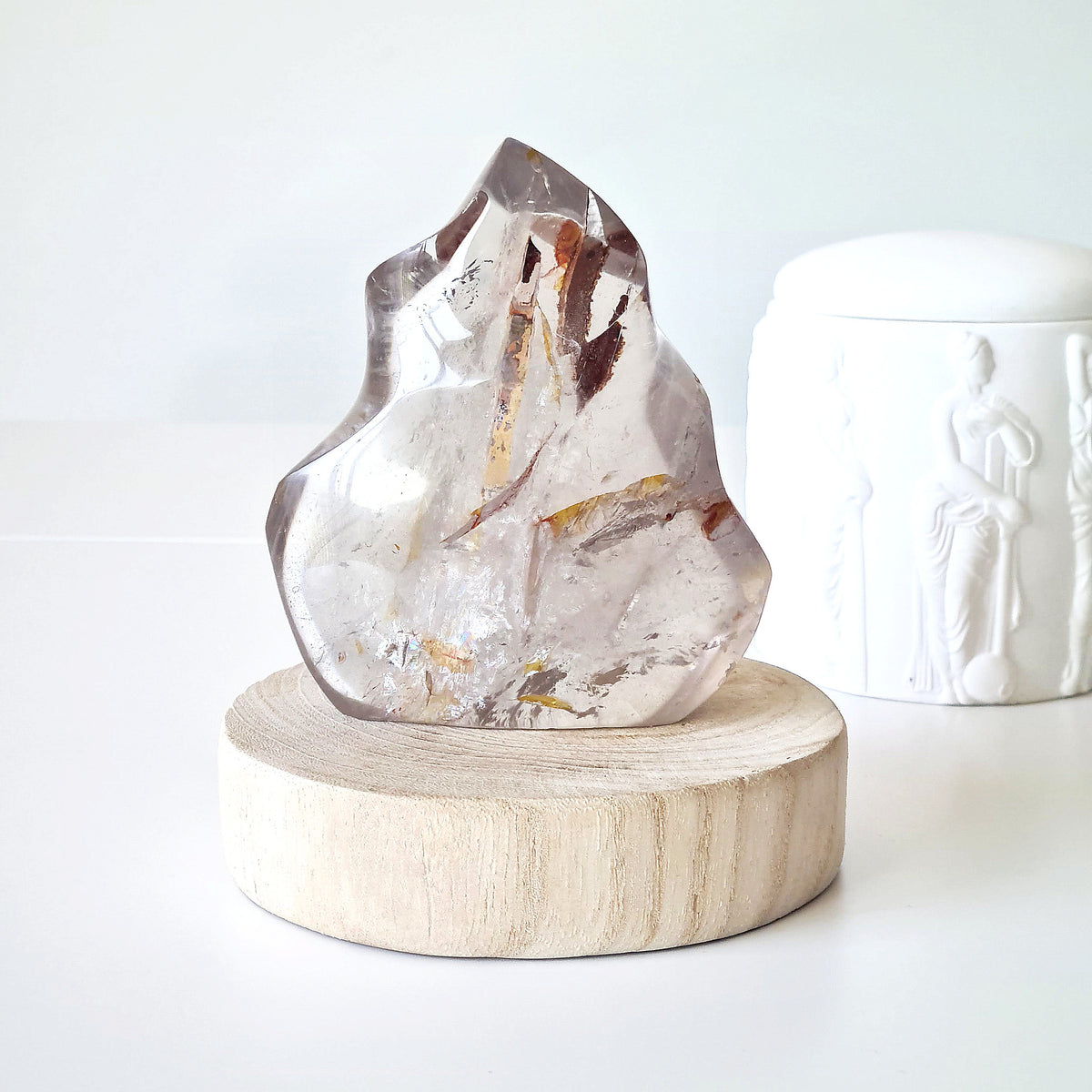 Polished quartz flame with smoky brown inclusions and a natural pocket, displayed on a round wooden base.